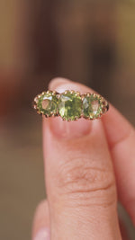 A video of a green zircon three-stone ring in gold metal held between the fingers and turned to show different angles of the ring.