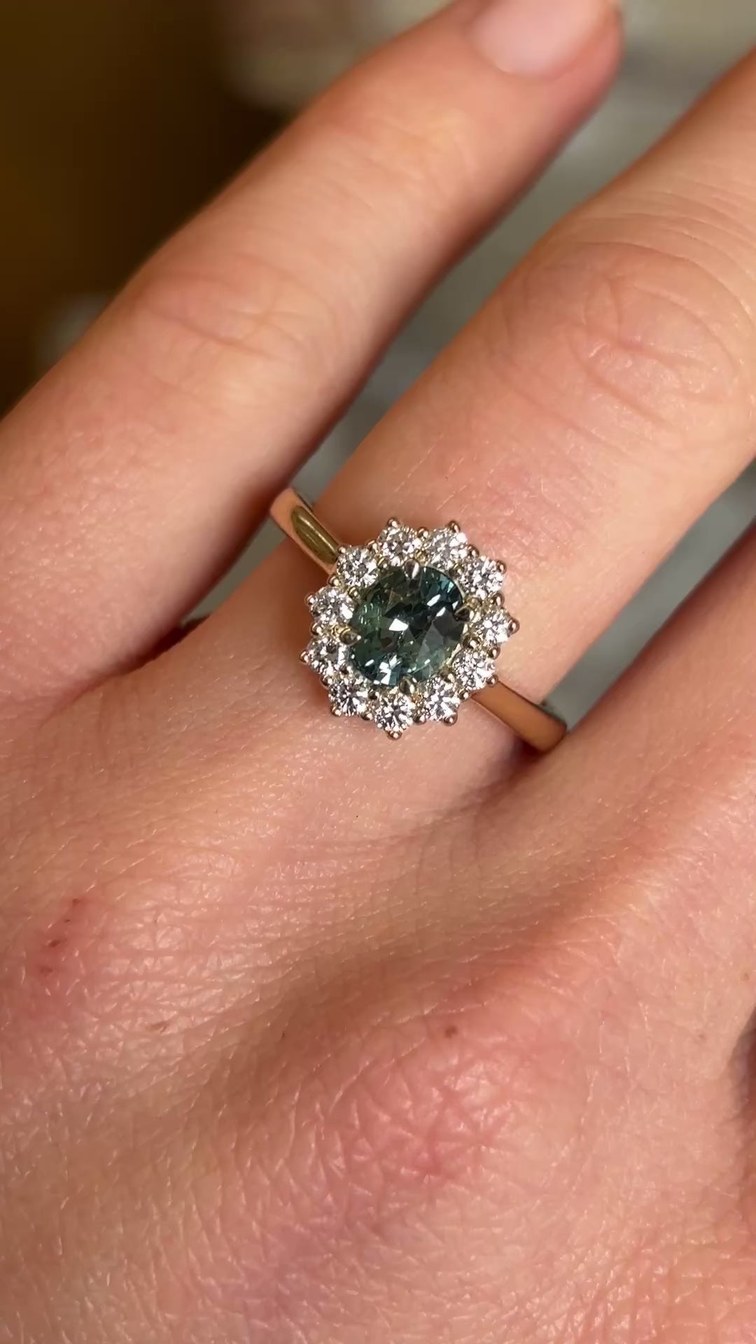 Green sapphire and diamond cluster engagement ring worn on hand and moved back showing size. 