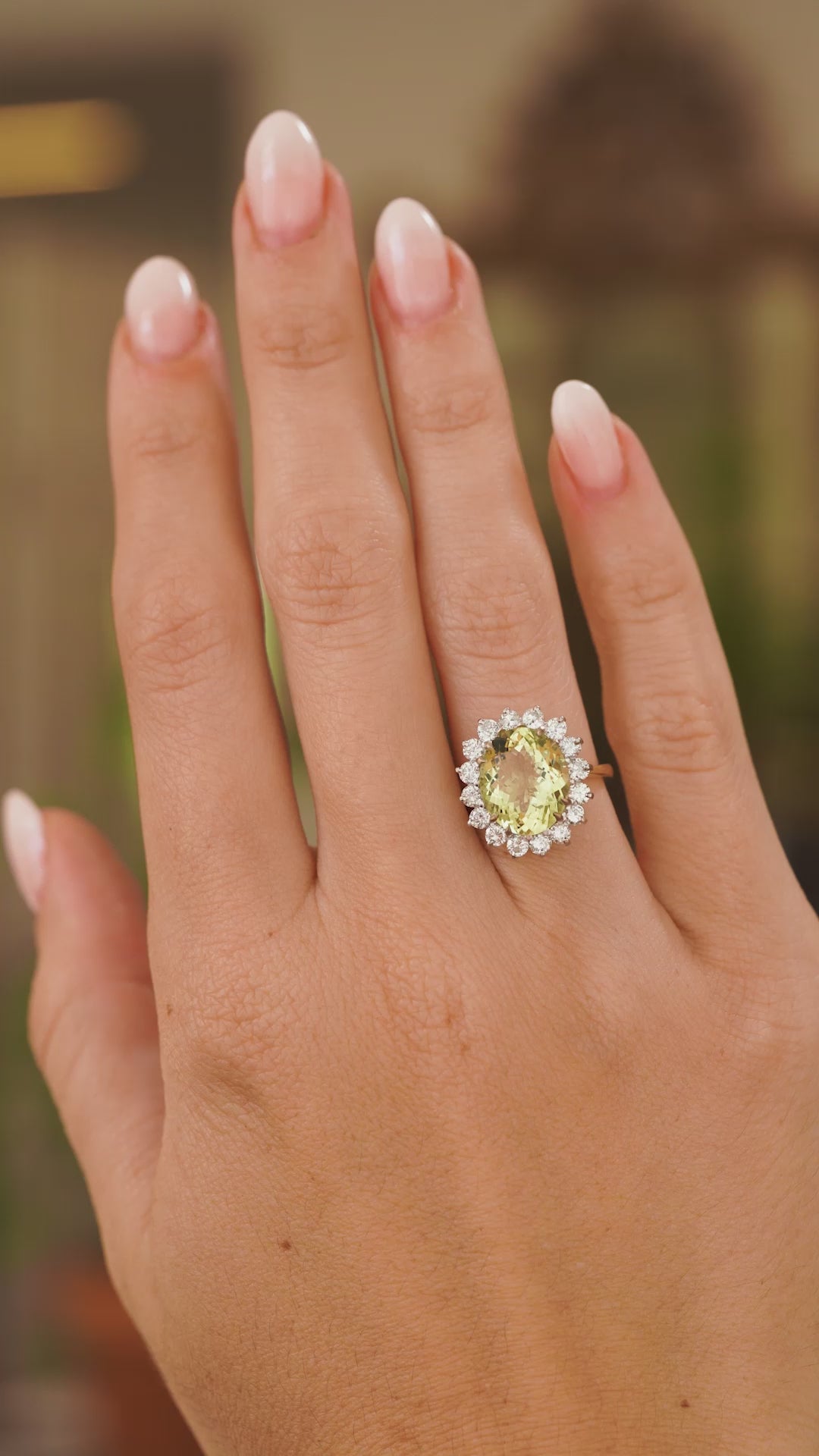 A video of an outstretched hand wearing a Vintage, 1960s Green beryl and diamond cluster engagement ring in yellow gold the hand slowly turns to show off the proportions
