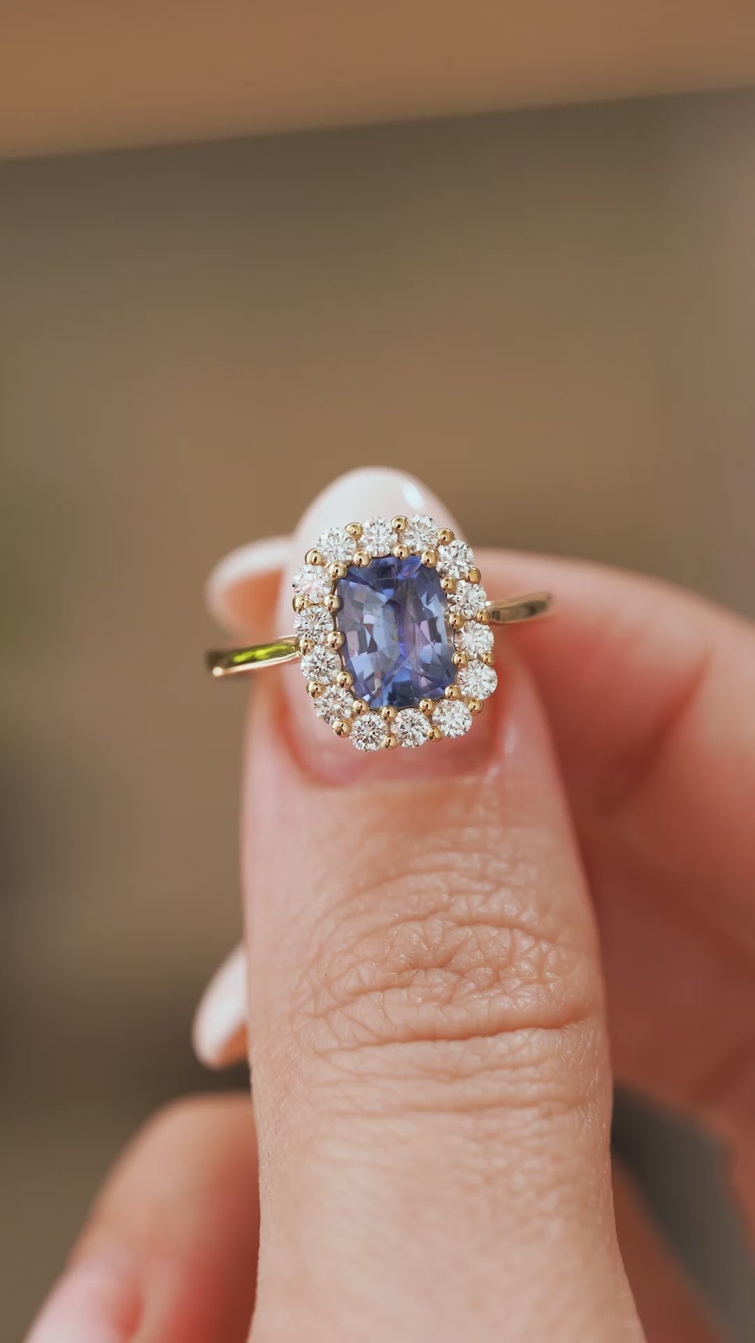 Video close-up of a vintage-inspired blue sapphire cluster ring balanced on a fingertip, highlighting the diamond halo and yellow gold setting.