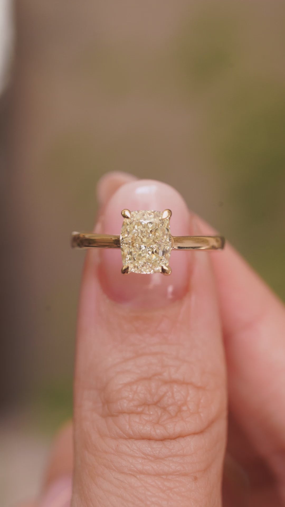 A video Antique-inspired, cushion-cut diamond solitaire engagement ring in yellow gold held in between fingers and slowly rotated