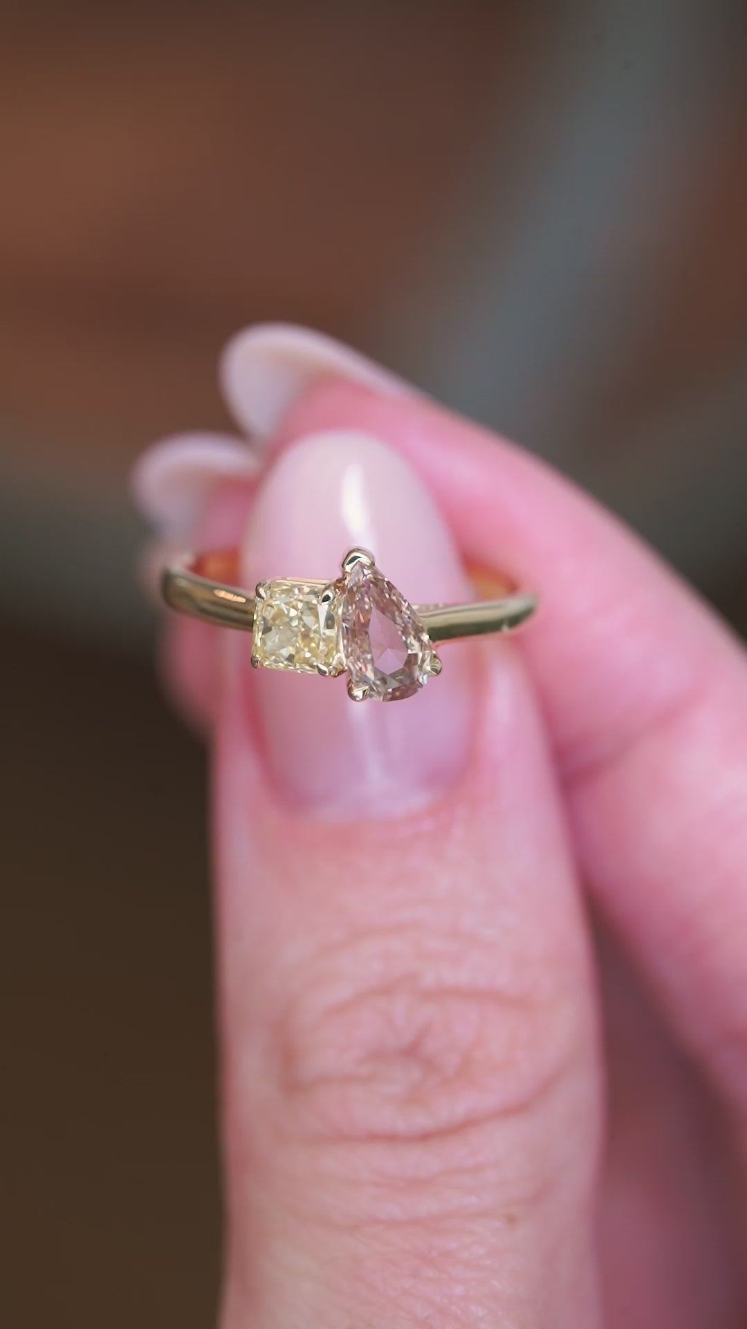 Brown and yellow diamond Toi et Moi engagement ring held between fingers showing ring detail.