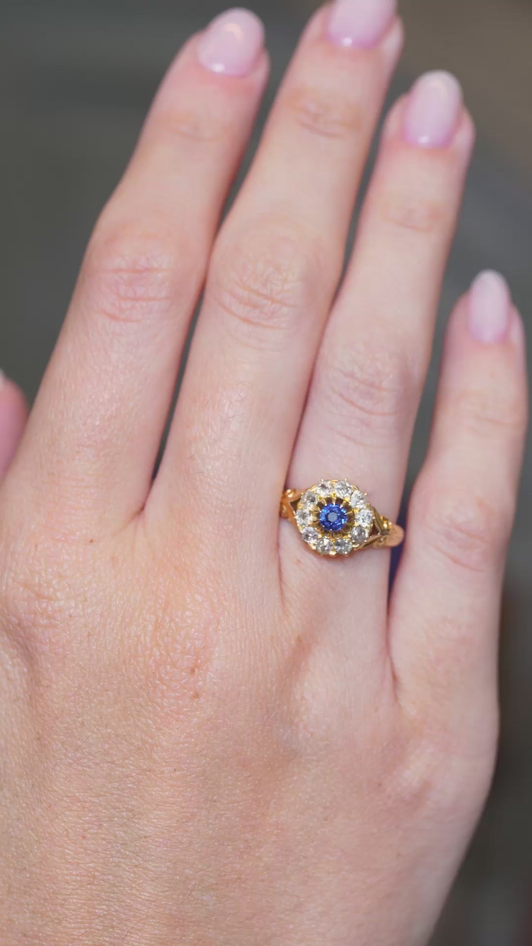 A video of an outstretched hand wearing an Antique, Victorian blue sapphire and old mine-cut diamond yellow gold cluster engagement ring whilst the fingers move.