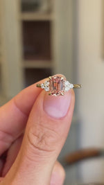 A Vintage-inspired yellow gold engagement ring shown in a close-up video held between two fingers, displaying the sapphire gemstone at the centre and diamond trefoil shoulders.