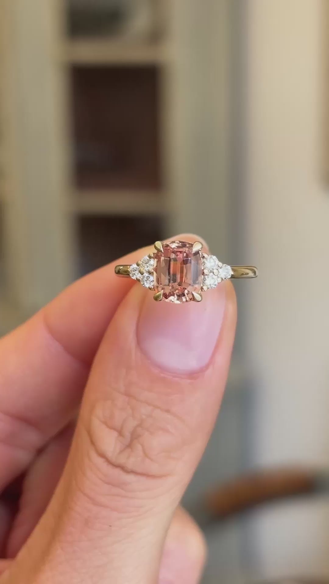 A Vintage-inspired yellow gold engagement ring shown in a close-up video held between two fingers, displaying the sapphire gemstone at the centre and diamond trefoil shoulders.