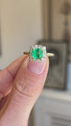Vintage 1980s Colombian emerald and diamond cluster engagement ring featuring an emerald-cut Colombian emerald surrounded by a halo of brilliant-cut diamonds, displayed on a hand.