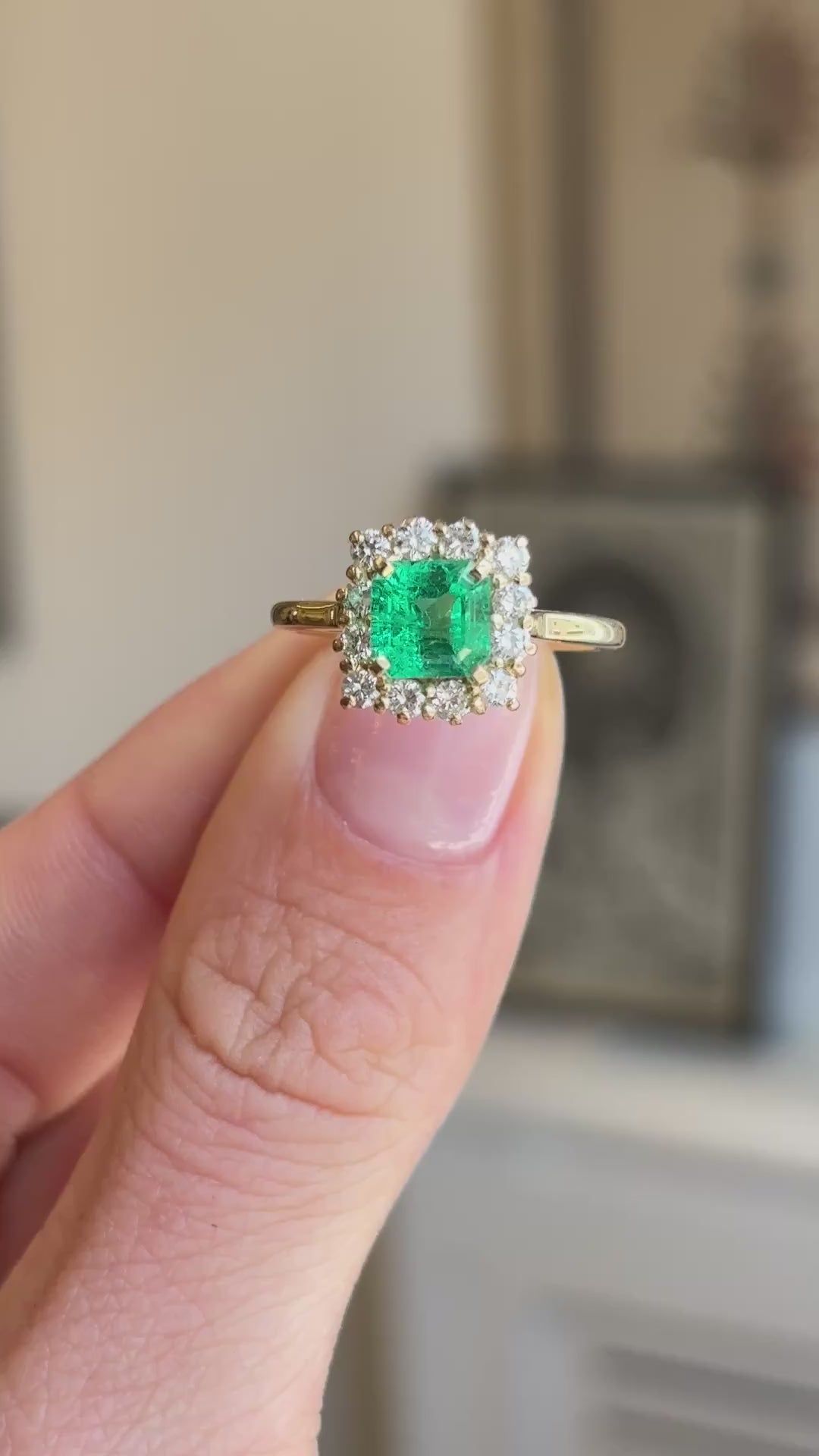 Vintage 1980s Colombian emerald and diamond cluster engagement ring featuring an emerald-cut Colombian emerald surrounded by a halo of brilliant-cut diamonds, displayed on a hand.