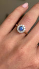 Video of a hand wearing an Antique-inspired, electric blue sapphire and diamond cluster engagement ring in yellow gold.