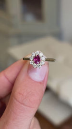 An antique-inspired engagement ring, with a ruby and diamond cluster in yellow gold shown between two fingers.