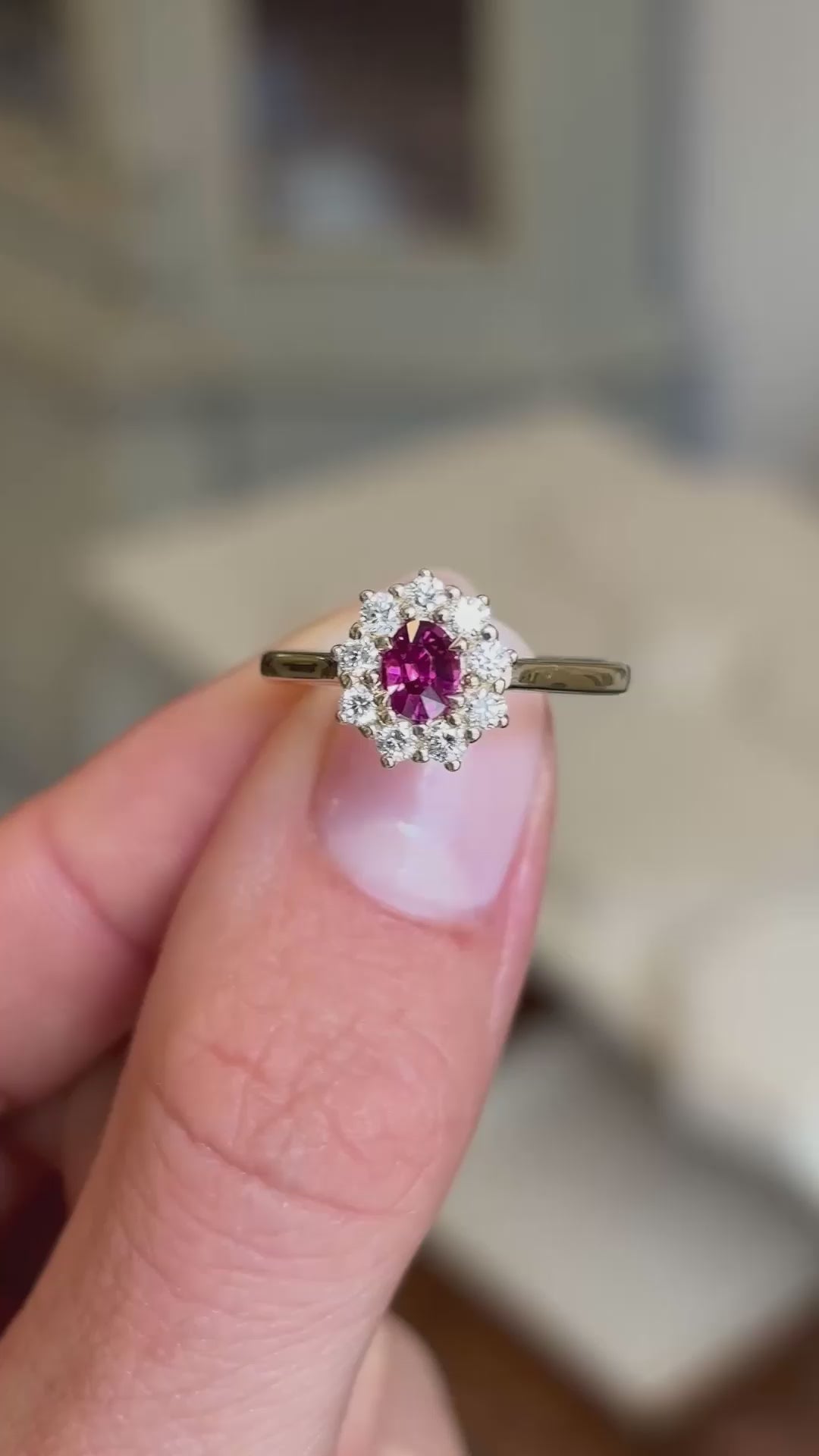 An antique-inspired engagement ring, with a ruby and diamond cluster in yellow gold shown between two fingers.