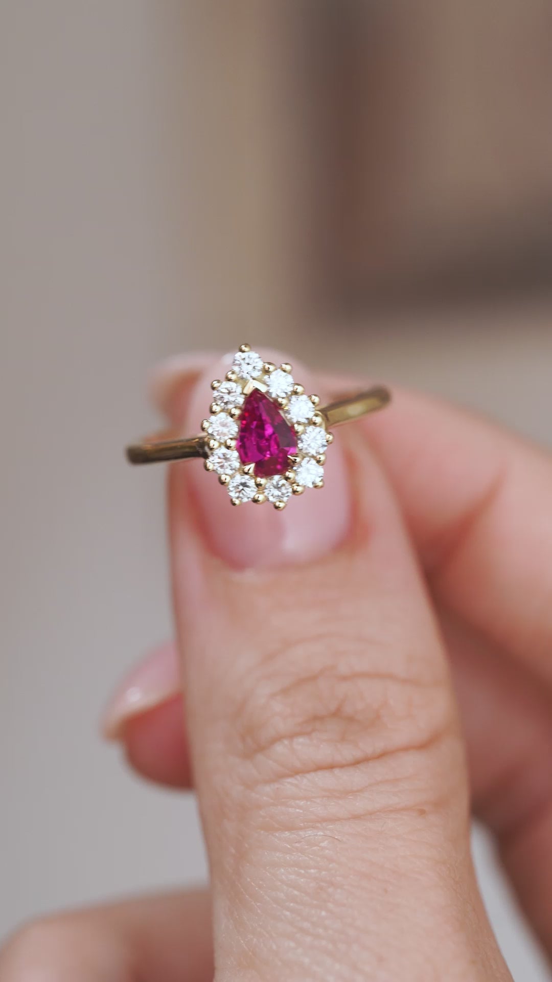 Video close-up of a pear-cut ruby and diamond halo ring balanced on a fingertip.