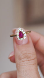 Video close-up of a pear-cut ruby and diamond halo ring balanced on a fingertip.