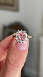 Antique-inspired sunset pink sapphire and diamond cluster engagement ring showcasing an octagon-cut sunset pink sapphire and diamond halo, held by hand to highlight the setting and craftsmanship.