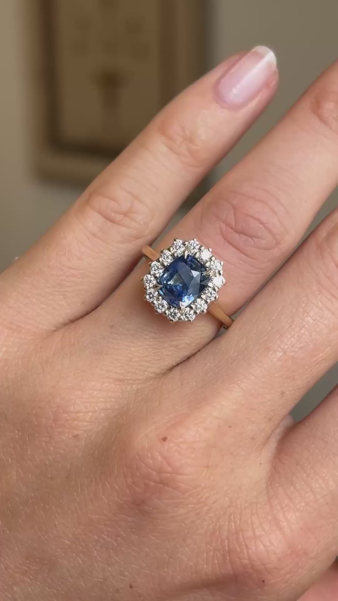 An Antique-inspired, cushion-cut sapphire and diamond cluster engagement ring in yellow gold shown on a finger in video.