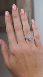A video of a vintage 1950s diamond cluster engagement ring worn on a hand, showcasing the sparkling floral diamond arrangement and delicate white gold band.