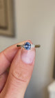 A three-stone antique inspired engagement ring held between two fingers and rotated slowly to showcase the central blue sapphire and two flanking diamonds.  