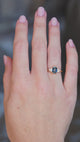 A hand wearing a teal sapphire and diamond trefoil engagement ring in yellow gold.