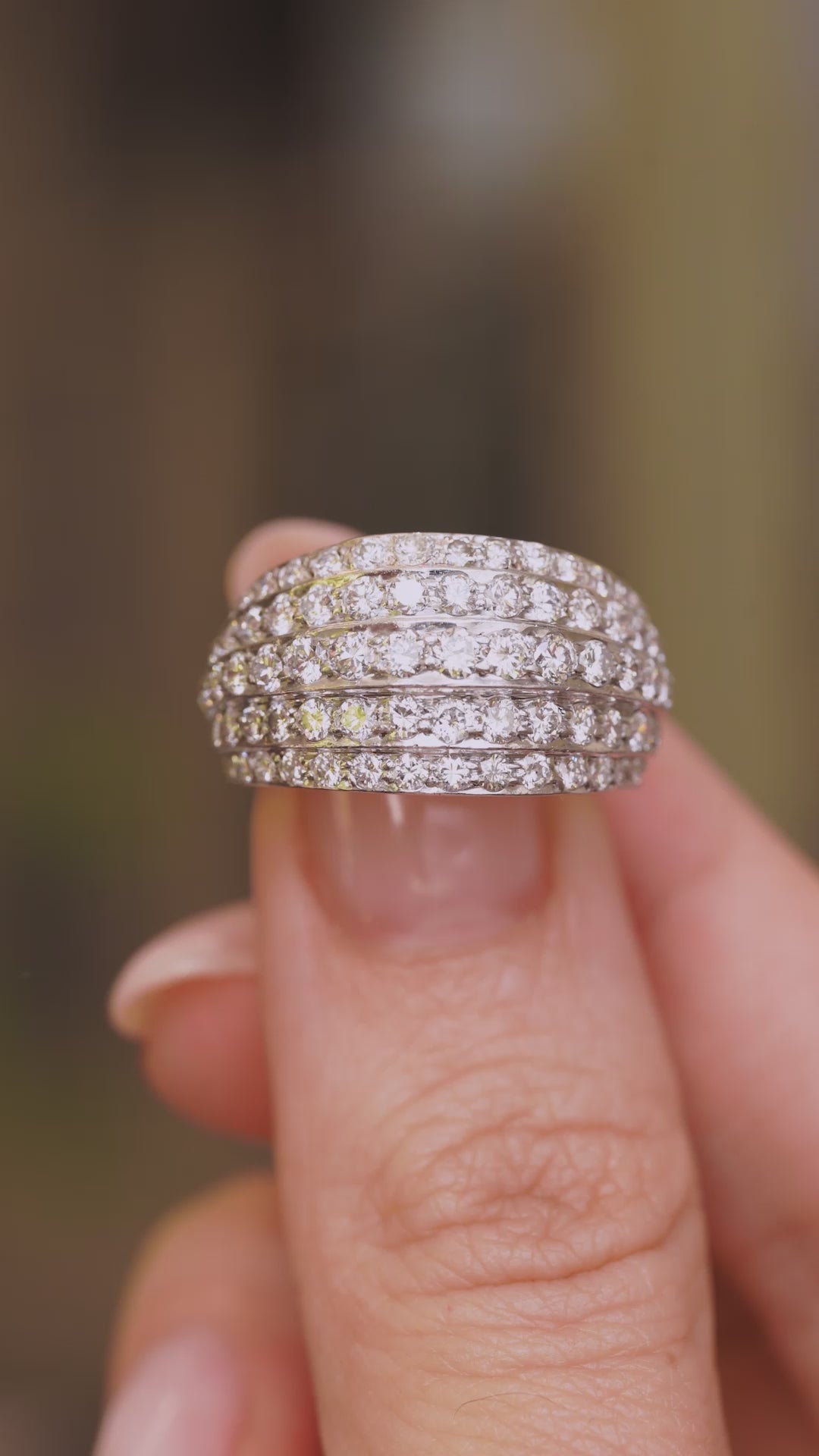 a video of A Vintage, 1950s diamond bombe cocktail ring in white gold held in between the fingers against a blurry background.