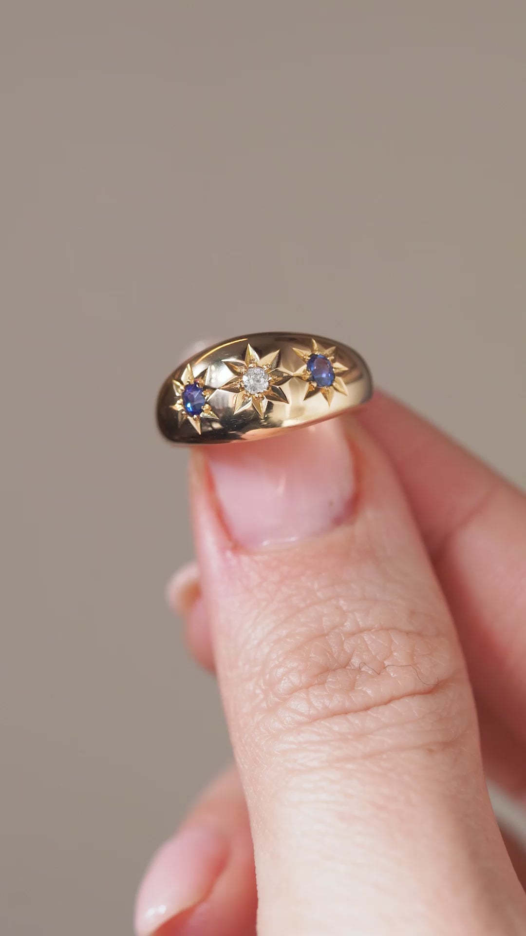 A close-up video showcasing the antique three-stone ring held between fingertips, capturing the sparkle of its gemstones and engraved star details.