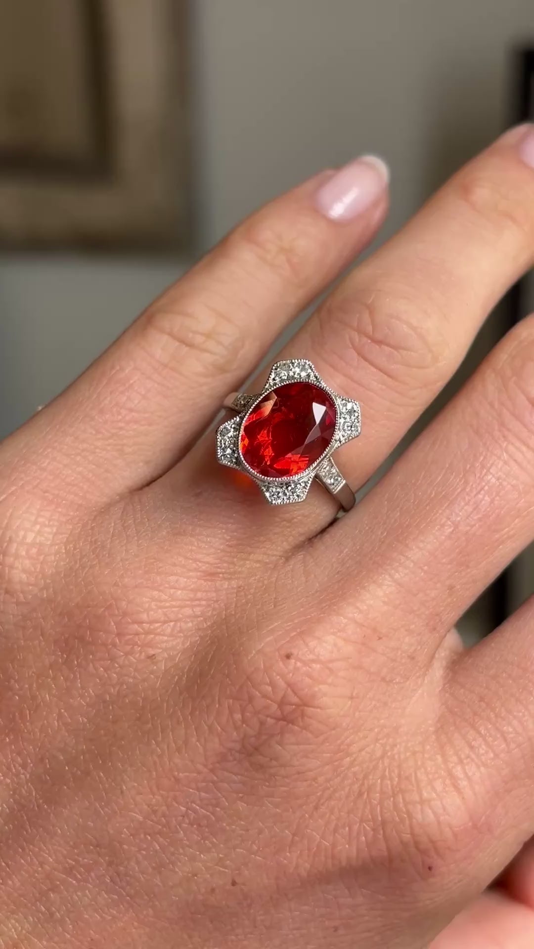 Antique Art Deco fire opal and diamond cluster ring featuring a vibrant fire opal surrounded by a halo of diamonds, displayed on a hand.