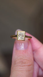 Video of a Vintage-inspired, princess-cut diamond rub-over solitaire engagement ring in yellow gold, held between two fingers and rotated to see all angles.