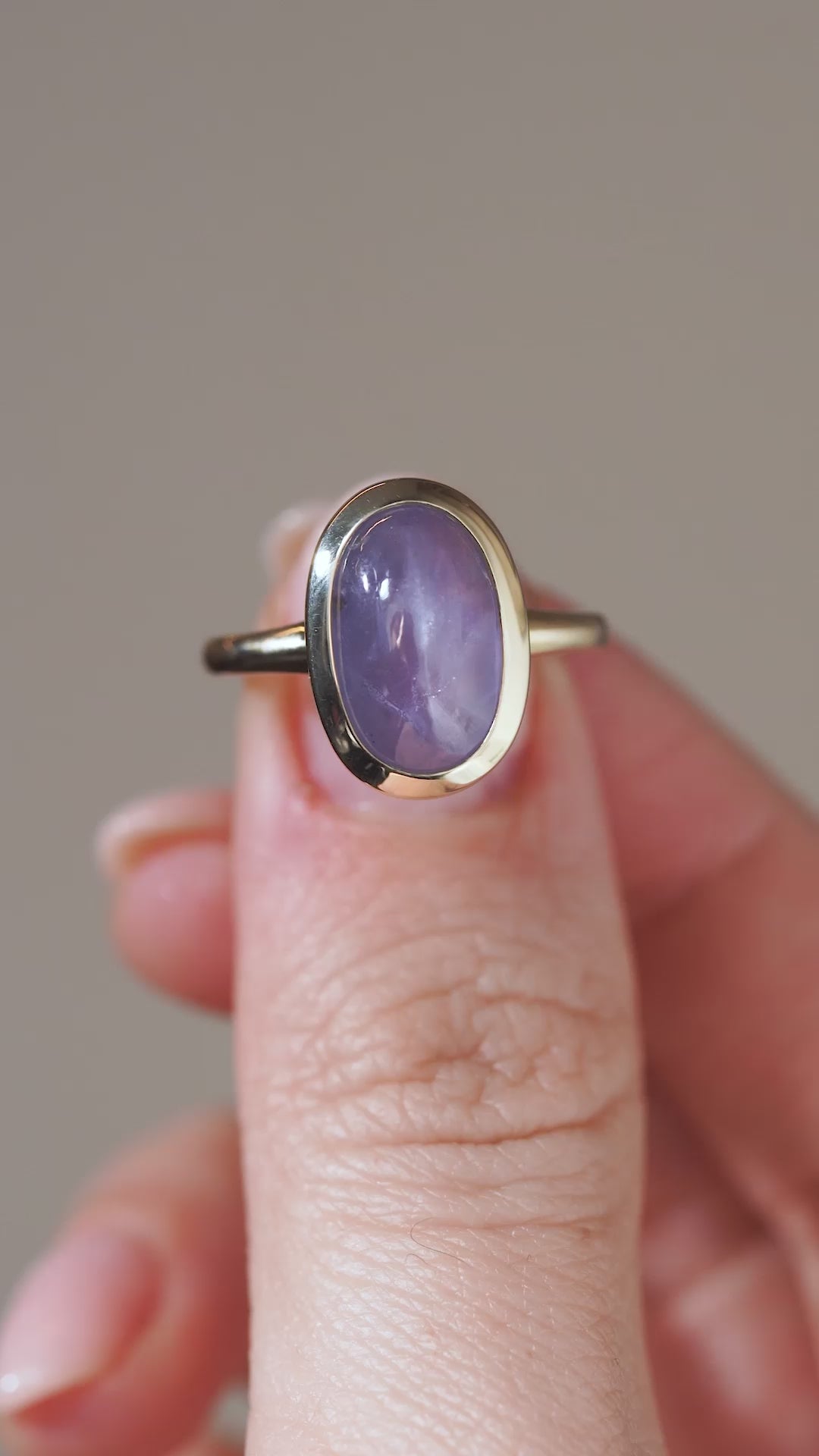 A close-up video showing the sapphire solitaire held between fingertips, revealing its subtle band of light and gentle colour variations.