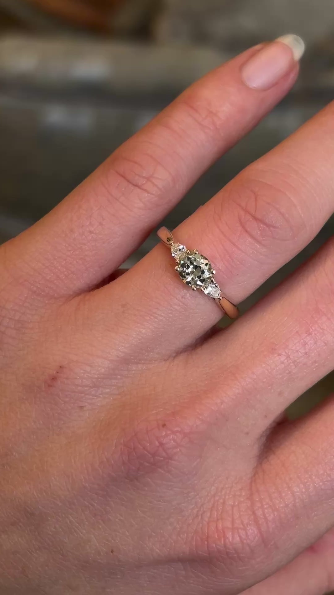 Diamond three-stone engagement ring worn on hand and moved to show diamond scintillation and scale. 