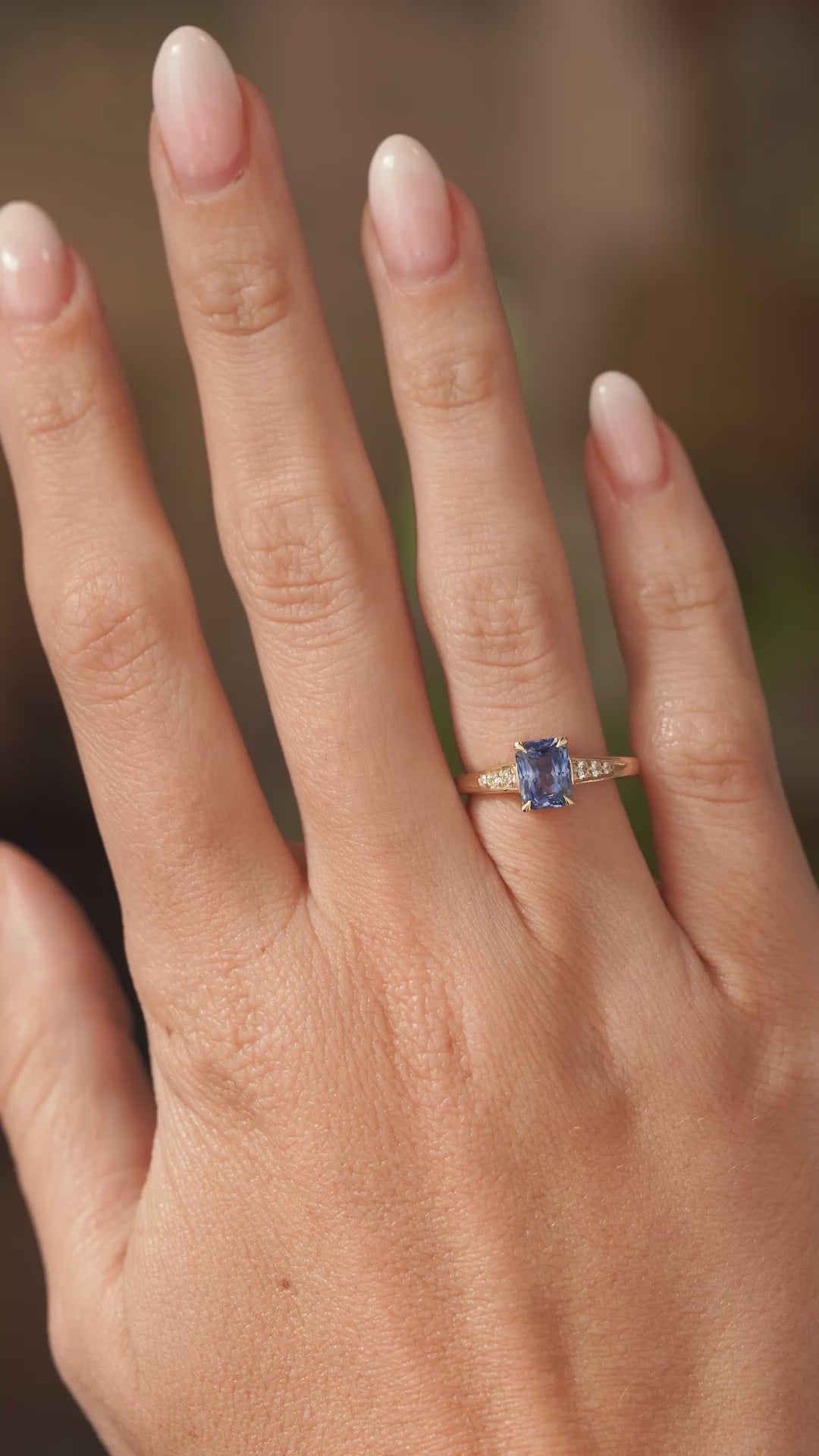 A video of a natural blue sapphire flanked by diamond set shoulders in a vintage inspired yellow gold engagement ring the hand slowly turns to show the proportions of the ring.