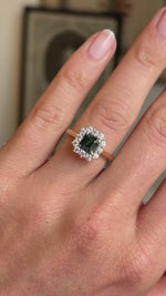 A close-up of a hand wearing an antique-inspired ring with a green rectangular centre sapphire surrounded by a halo of diamonds on a yellow gold band shown in video.