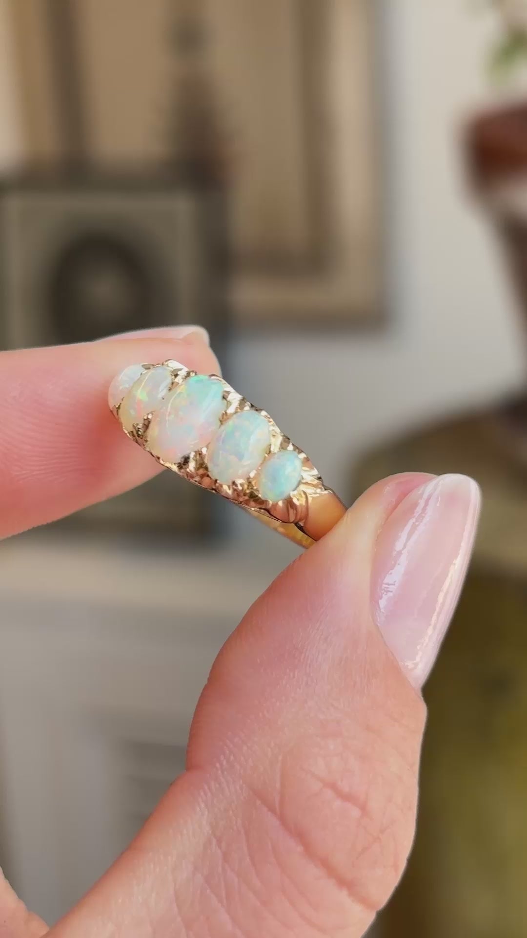 A close-up video of an Antique, Victorian Australian precious opal five-stone ring in yellow gold held between fingers.