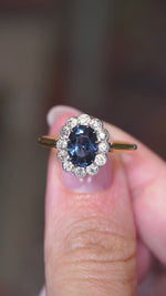 A video of an Antique, Edwardian blue spinel surrounded by a halo of diamonds in a coronet cluster engagement ring in yellow gold held in the hand and turned to showcase different angles. 