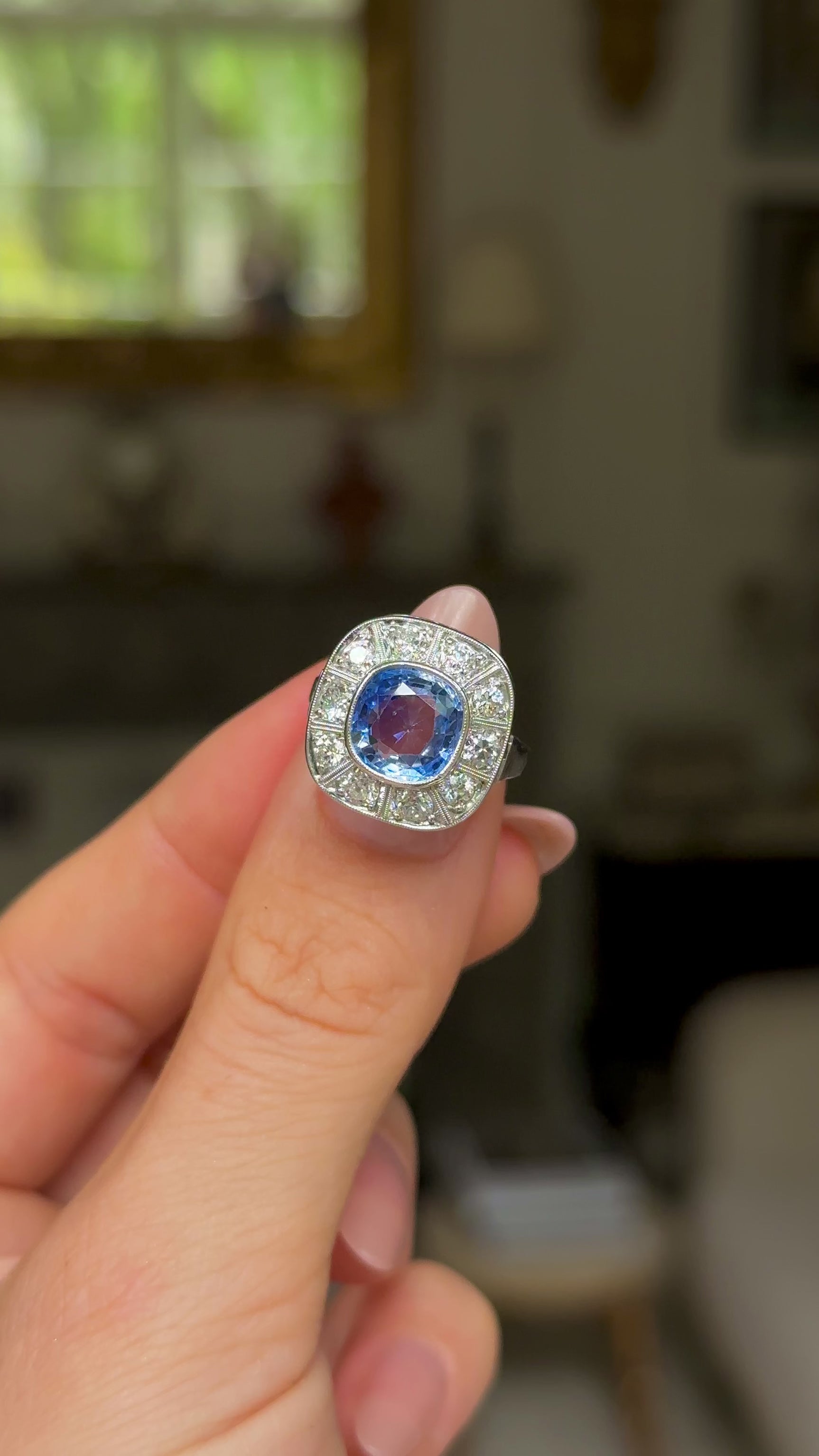 Art Deco, ceylon cushion-cut sapphire and diamond cluster ring, held in fingers and rotated to give perspective.