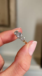Close up video of an Antique, Edwardian gold three-stone ring, held between two fingers and rotated slowly to display the old-cut diamonds. 
