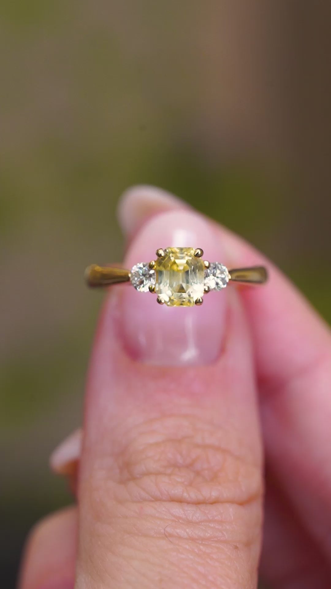 A video of a vintage-inspired yellow sapphire and diamond three-stone ring in yellow gold held between fingers shown in video.