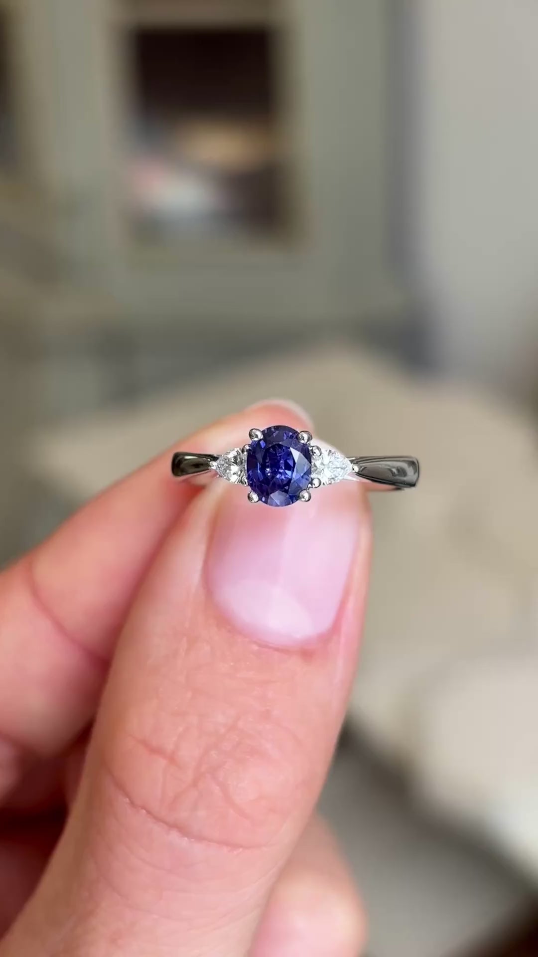 Close up video of a Vintage-inspired, indigo sapphire & diamond three-stone engagement ring in platinum held between two fingers and rotated slowly to showcase it from all angles