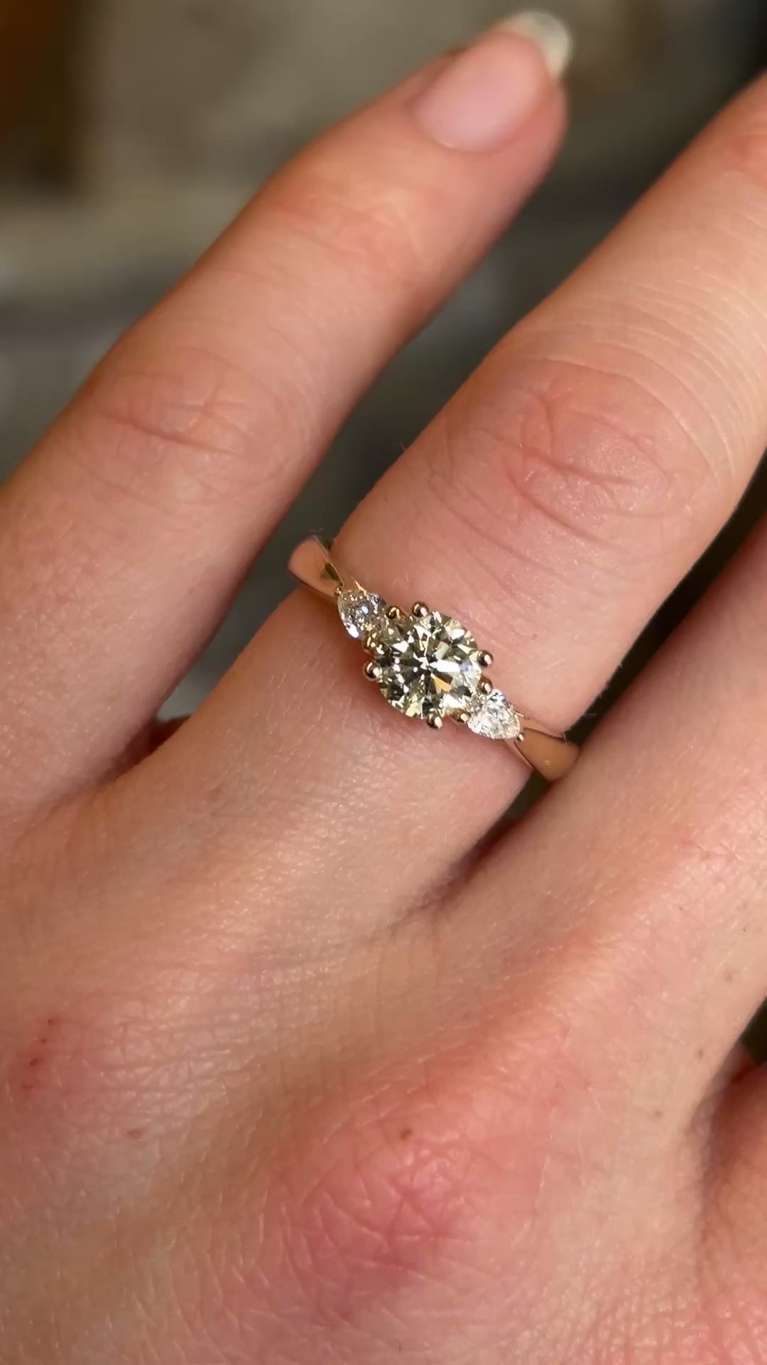 Round cut and pear-cut diamond three-stone yellow gold engagement ring at a distance on hand showing size. 