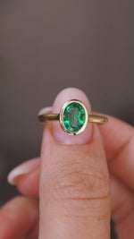 A close up video of an Antique-inspired, Emerald solitaire engagement ring rotated slowly to showcase the yellow gold bezel setting and band. 