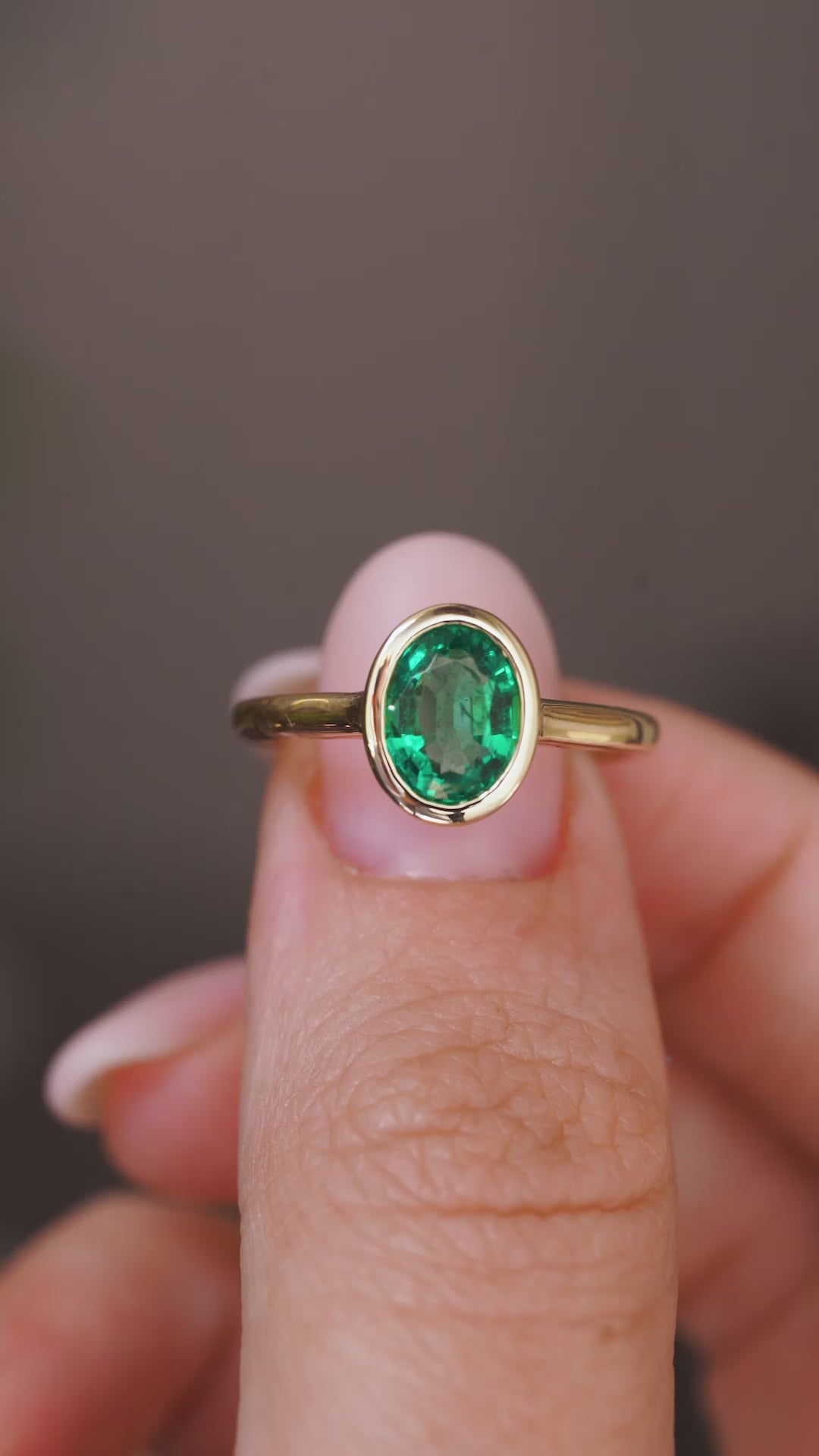 A close up video of an Antique-inspired, Emerald solitaire engagement ring rotated slowly to showcase the yellow gold bezel setting and band. 