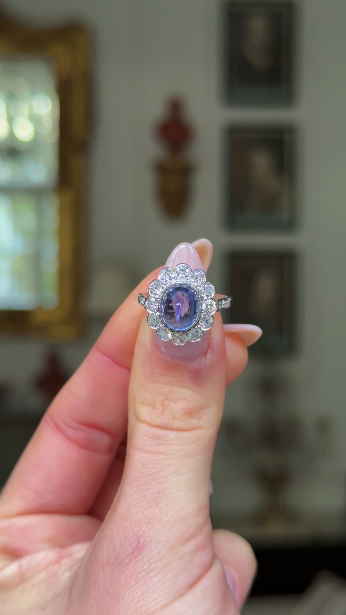 cabochon sapphire and diamond cluster ring set in platinum held in fingers and rotated to give perspective.