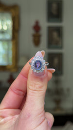 cabochon sapphire and diamond cluster ring set in platinum held in fingers and rotated to give perspective.