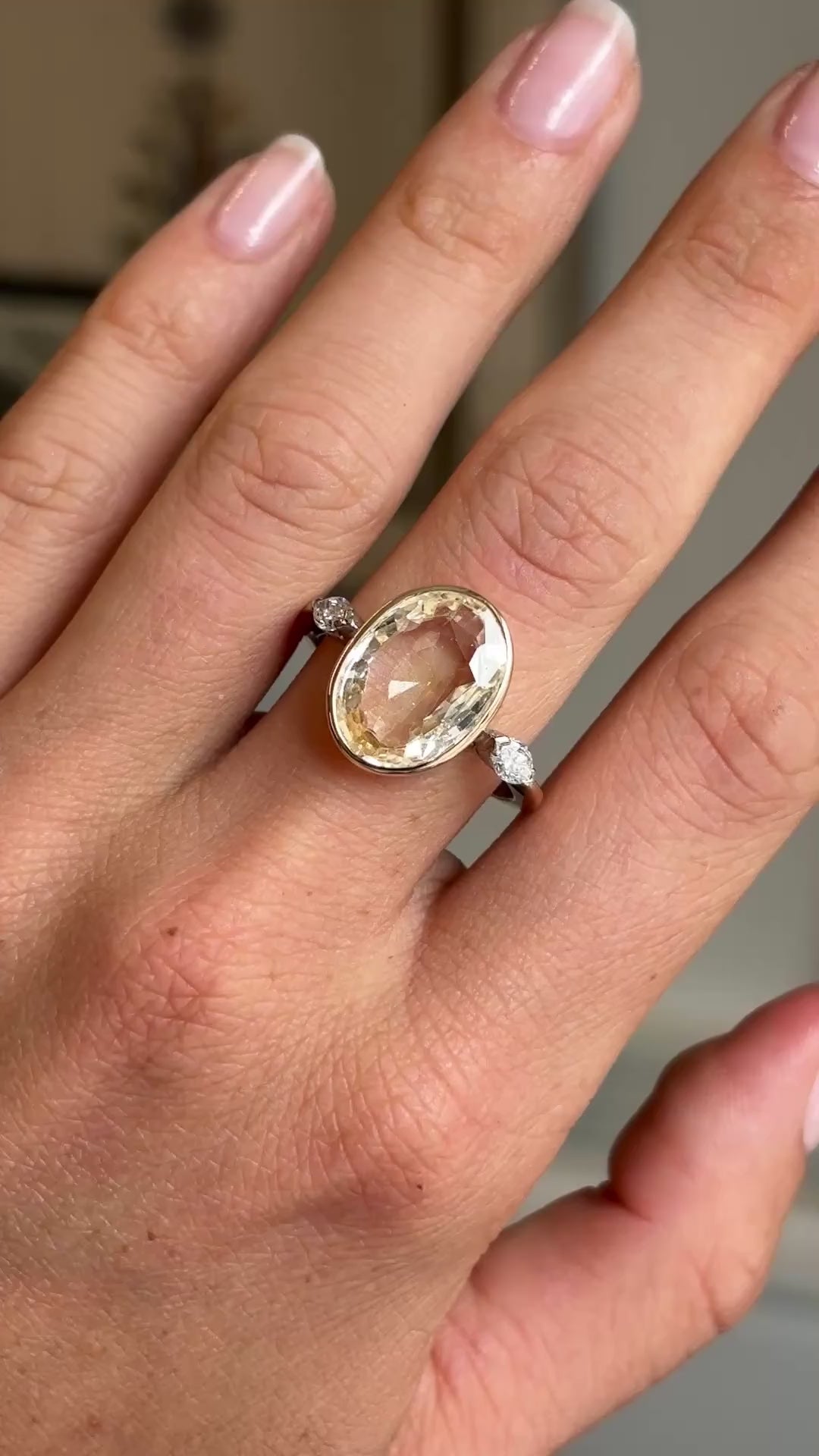 Video of a yellow gold Vintage, 1980s yellow sapphire & diamond three-stone engagement ring worn on a hand against a blurred background