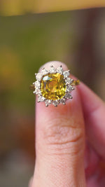 A vintage-inspired, yellow sapphire and diamond cluster engagement ring held between fingers to show the details of the ring from different angles.