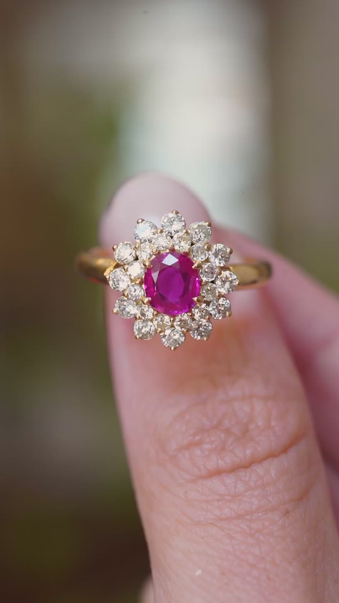 A video of a. vintage 1980s Burmese ruby and diamond cluster ring held between the fingers.