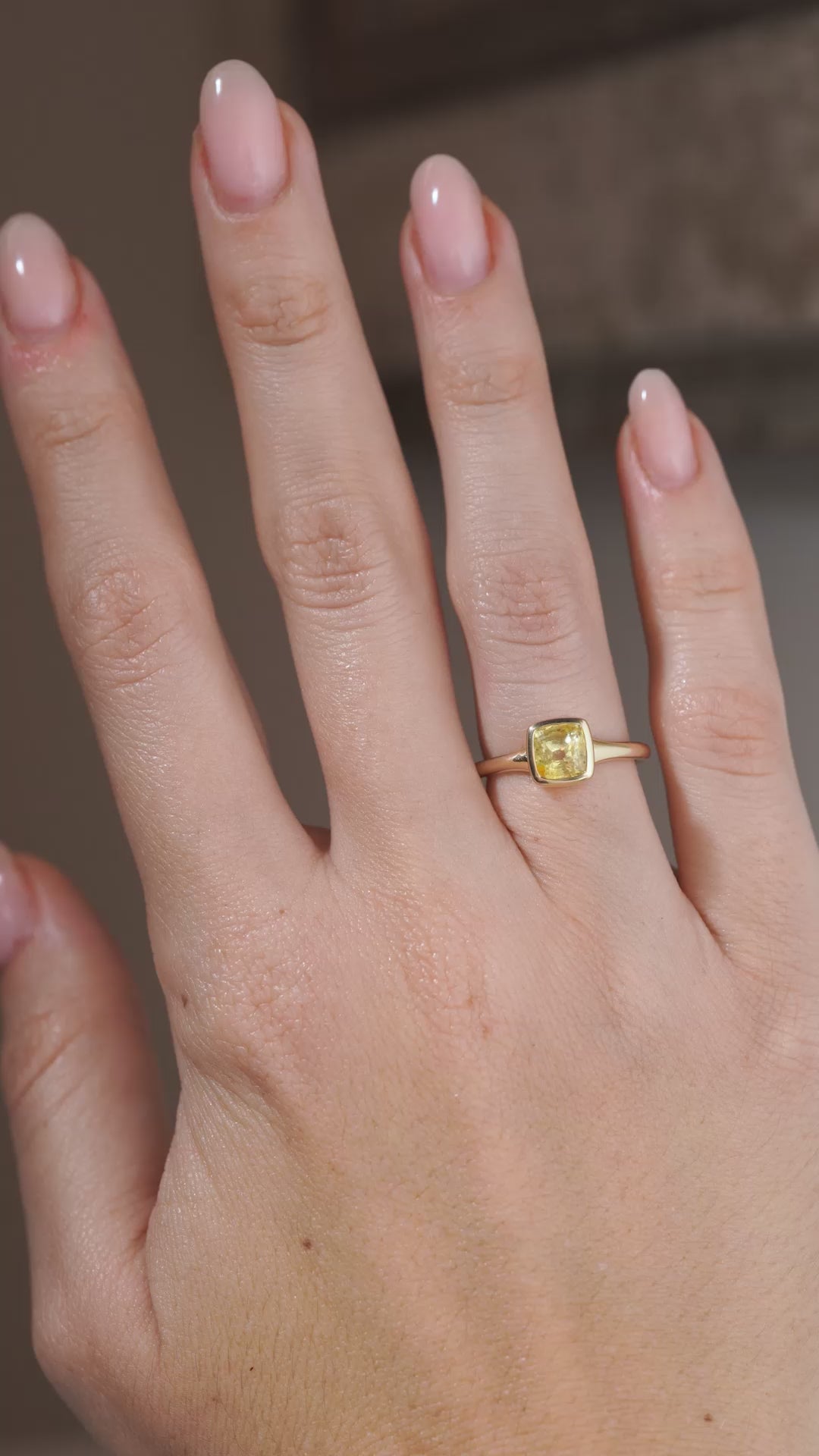 A video of a yellow sapphire solitaire engagement ring worn on a hand, capturing the gemstone's sparkle and polished yellow gold setting.