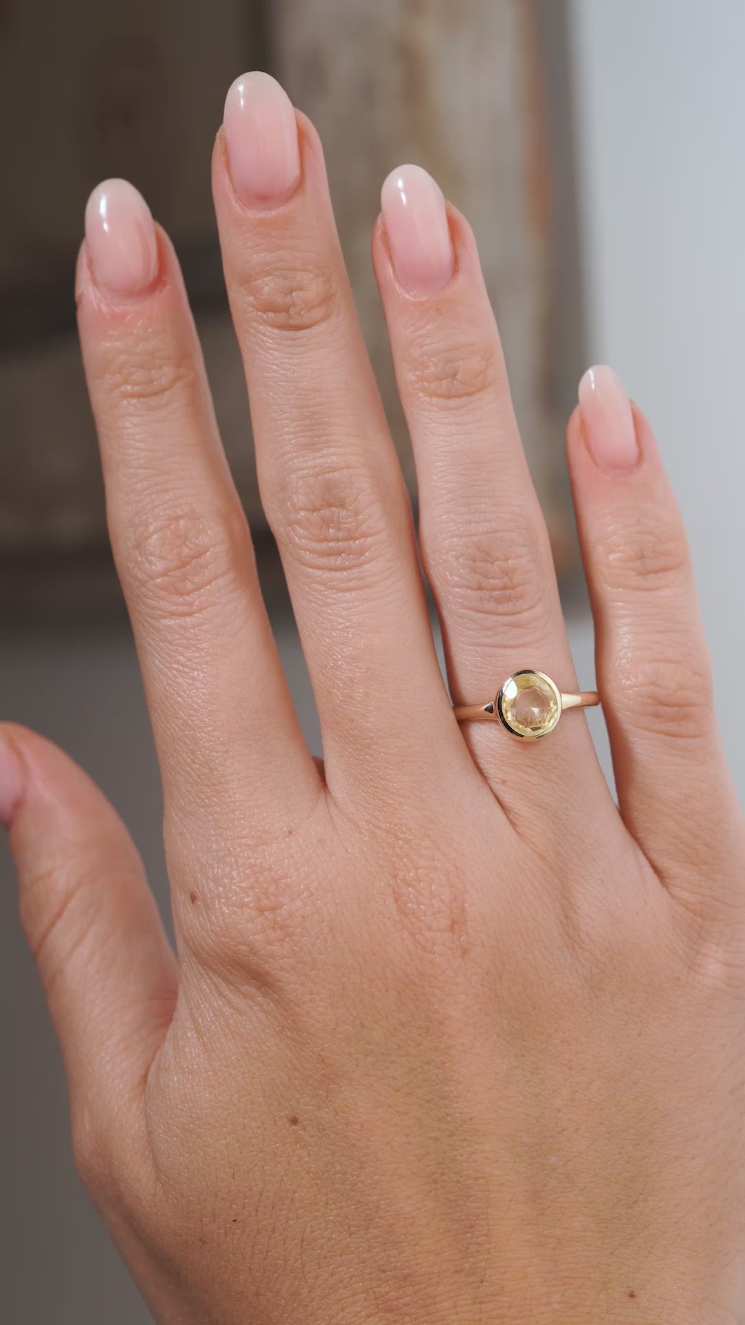 A video of an antique-inspired pale yellow sapphire solitaire engagement ring worn on a hand, showcasing the oval gemstone, minimalist bezel setting and polished yellow gold band.