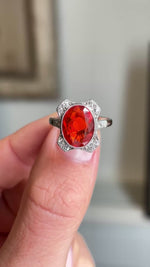 Antique Art Deco fire opal and diamond cluster ring showcasing a vivid fire opal and diamond halo, held by hand to highlight the setting and craftsmanship.
