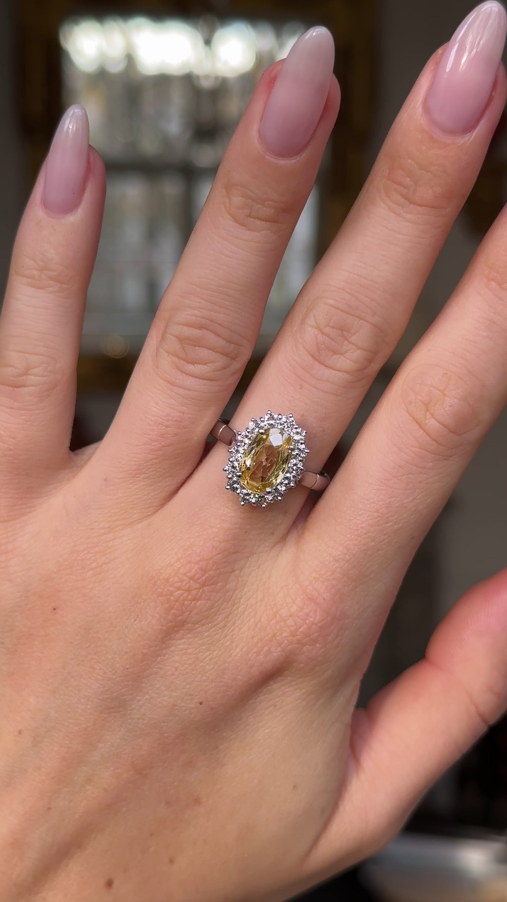 Yellow sapphire and diamond cluster engagement ring, worn on hand and rotated to give perspective.
