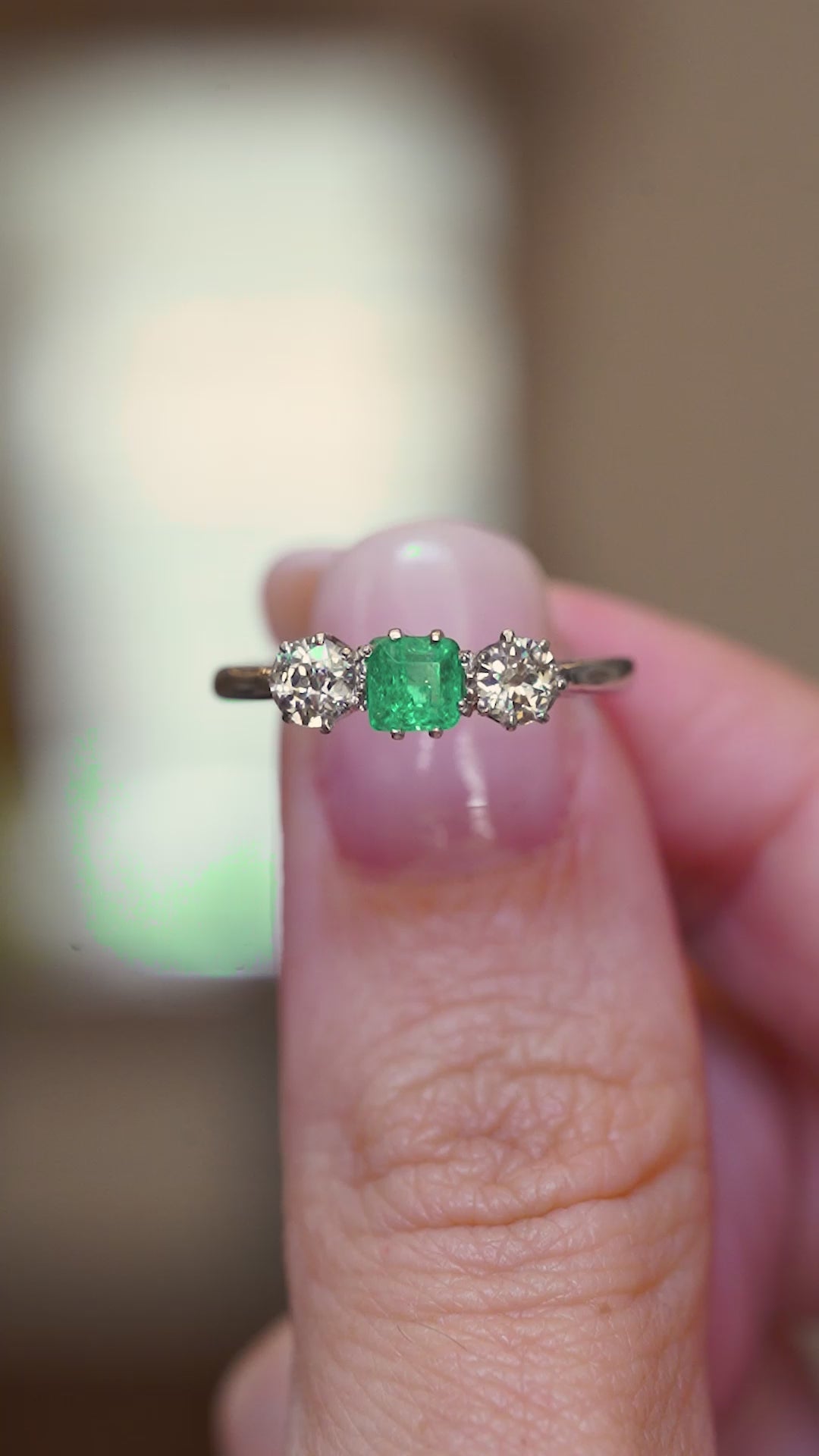 A video of an Antique ring held between two fingers showcasing its details, featuring an emerald at its centre and old-cut diamonds.