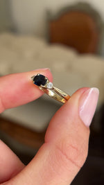 Video of a gold vintage 1960s three-stone ring, set with a midnight blue sapphire flanked by two diamonds, held between two fingers