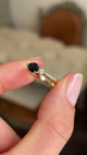 Video of a gold vintage 1960s three-stone ring, set with a midnight blue sapphire flanked by two diamonds, held between two fingers